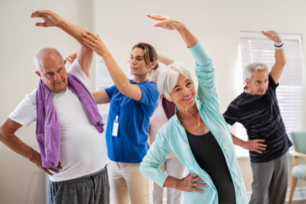 personas de la tercera edad que se estiran con el entrenador en la comunidad de jubilados - atención residencial fotografías e imágenes de stock