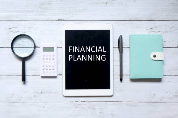 istock Top view of magnifying glass,calculator,pen,notebook and tablet computer written with 'FINANCIAL PLANNING' on white wooden background. 1316205633