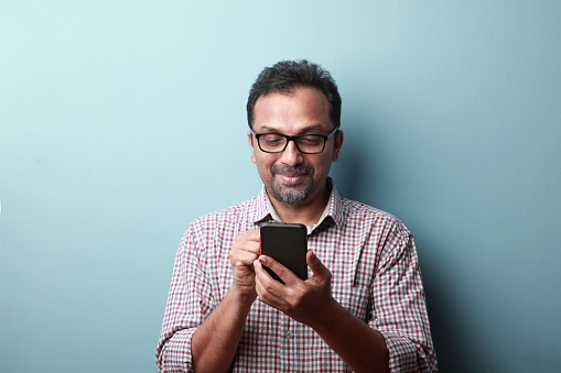 Hombre de mediana edad de origen indio mirando su teléfono móvil con una sonrisa photo
