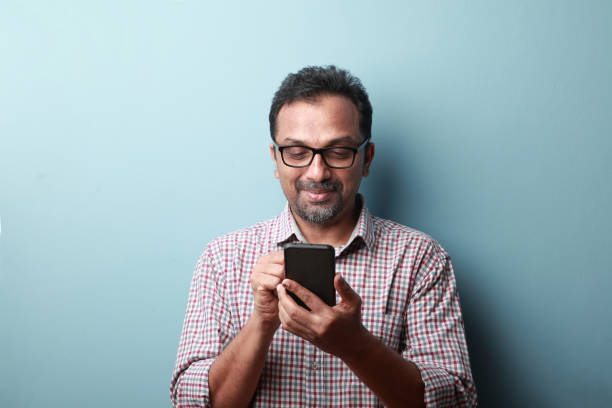 mężczyzna w średnim wieku pochodzenia indyjskiego patrząc na jego telefon komórkowy z uśmiechem - mustache ethnic asian ethnicity men zdjęcia i obrazy z banku zdjęć