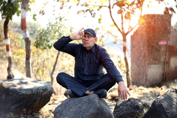 Indian senior men sitting on rock and doing yoga outdoors in fresh near Patalpani Waterfall Location, Indore, India.