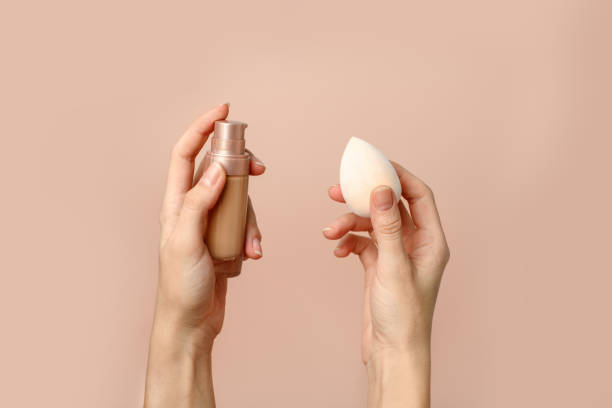 istock Applying foundation on makeup sponge. Woman's hands with neutral manicure holding bottle of concealer or toner foundation, cream and beauty blender, make up artist background 1316208811