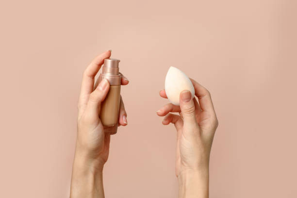 Applying foundation on makeup sponge. Woman's hands with neutral manicure holding bottle of concealer or toner foundation, cream and beauty blender, make up artist background Applying foundation on makeup sponge. Woman's hands with neutral manicure holding bottle of concealer or toner foundation, cream and beauty blender, make up artist background make up brush photos stock pictures, royalty-free photos & images