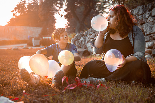 Siblings seating on a grass and having fun with balloons