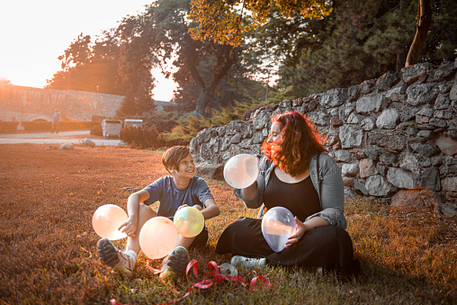 Siblings seating on a grass and having fun with balloons