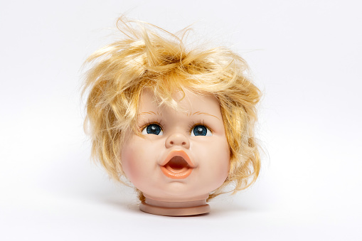 Head of an old girl doll with tousled blond hair against a white background