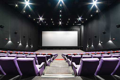Empty big movie theater hall with a white screen for copy space. Wide angle view of the purple seats and the room, looking at the screen.