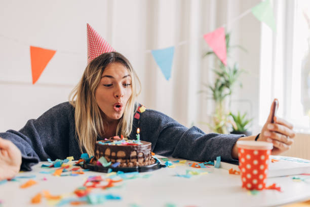 Woman celebrating birthday alone One woman, beautiful young woman using smart phone for selfie, she is celebrating her birthday alone at home. woman birthday cake stock pictures, royalty-free photos & images