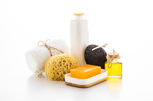 Front view of various shower products such as a shampoo, a pumice stone, a towel, a bath sponge and a bar of soap isolated on white background.