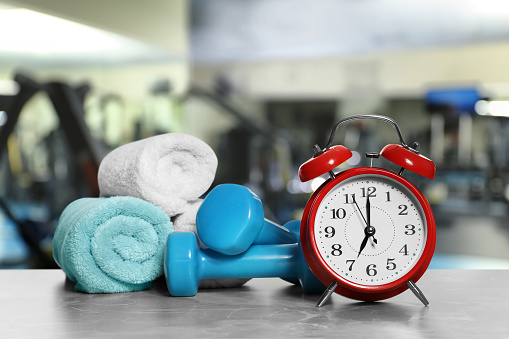 Alarm clock, towels and dumbbells on marble surface in gym. Morning exercise