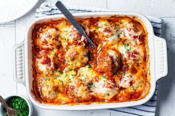 Baked cheesy meatballs casserole with tomato sauce in the oven dish.