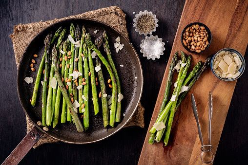 Pan fried asparagus served from the skillet. Cooked with a tiny bit of oil or butter just give a bit of colour and taste to the asparagus stems. Served with; pine nuts, vegan parmesan cheese and salt and pepper.Overhead view, horizontal format with some copy space.