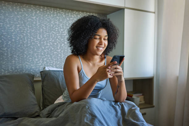istock Shot of a young woman using her cellphone while sitting on her bed 1316229400
