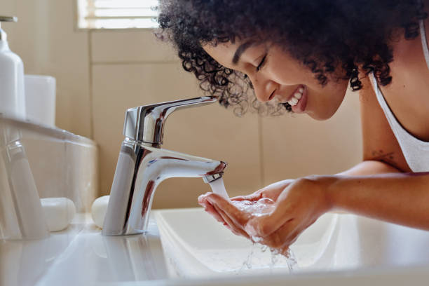 ontsproten van een mooie jonge vrouw die haar gezicht in de badkamers wast - gezicht wassen stockfoto's en -beelden