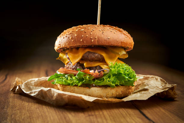 istock Juicy double burger with beef, salad, pickles, bacon and cheddar cheese, served on parchment on a wooden background. American fast food 1316235333