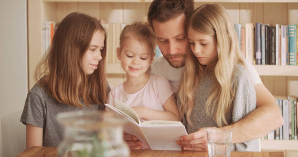 istock Family reading time. Father holding book and hugging his three daughters. 1316235510