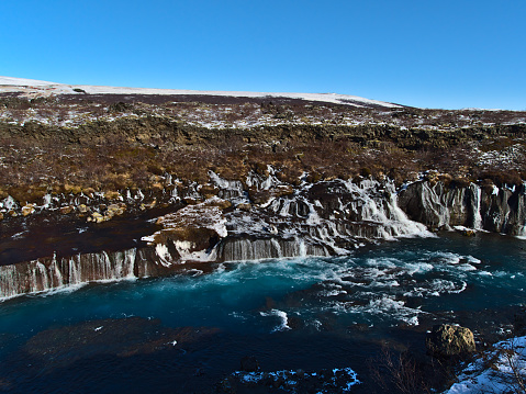 Stunning view of famous Hraunfossar cascades (Icelandic: lava waterfalls) near Húsafell in the west of Iceland on sunny winter day with raging river and turquoise colored water.