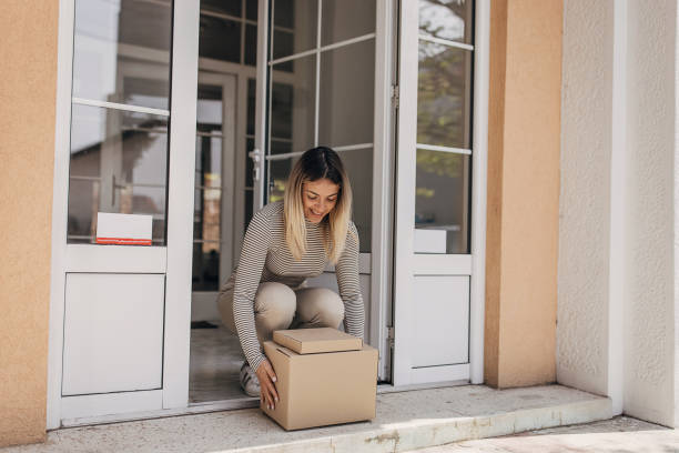 Woman picking up package One woman, female picking up cardboard boxes packages on front door that she just received. retrieving stock pictures, royalty-free photos & images