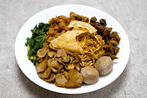 Delicious and Tasty Mie ayam or Mie Yamin or Yamin Noodle with chicken meat, vegetable, Pangsit Goreng, Pangsit rebus and meatballs on white plate