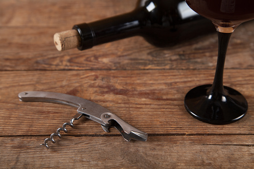 Bottle, glass and  wine with corkscrew on wooden background.