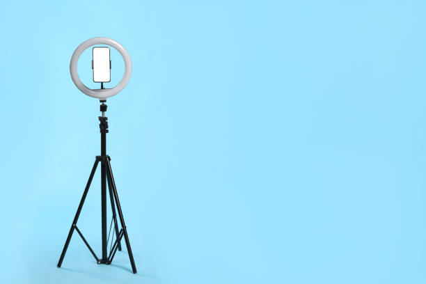 istock Modern tripod with ring light and smartphone on light blue background. Space for text 1316244835