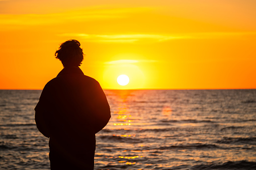 Stock photo showing close-up, profile view of unrecognisable male tourist, in silhouette, travelling on calm sea on a pleasure tour boat at sunset.