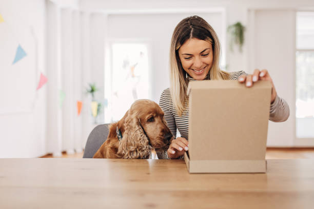 Woman opening a package One woman, female opening cardboard boxes package that she just received. Her dog is sitting next to her. package stock pictures, royalty-free photos & images