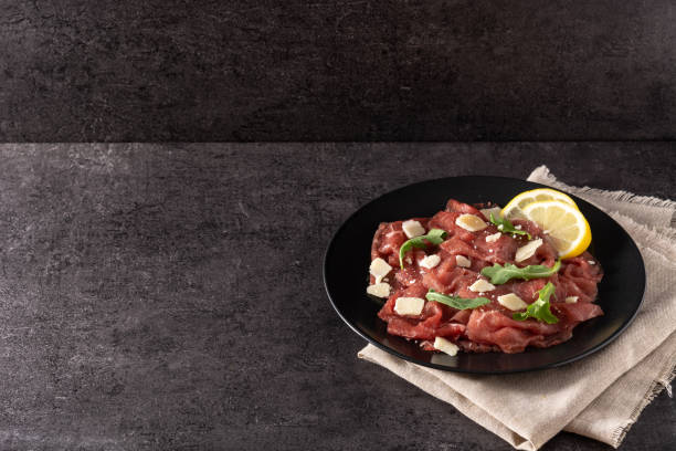 Marbled beef carpaccio on black plate Marbled beef carpaccio on black slate background carpaccio parmesan cheese beef raw stock pictures, royalty-free photos & images