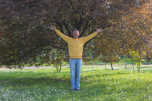 Man with arms outstretched standing on front of tree in springtime
