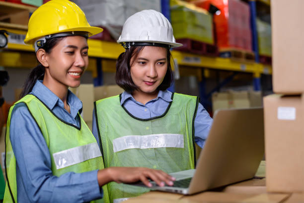 istock Warehouse woman wearing a hardhat standing cargo at goods or merchandise warehouse and check for control loading from Cargo freight ship for import and export by report on tablet. Teamwork concept 1316257800