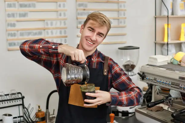 Photo of barista in apron pours fresh coffee into a cup