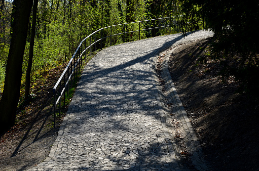 a new park path made of irregular cubes, folded with a side channel for draining water from the road surface. granite stones of gray and brown color in places the path is enclosed black metal railing