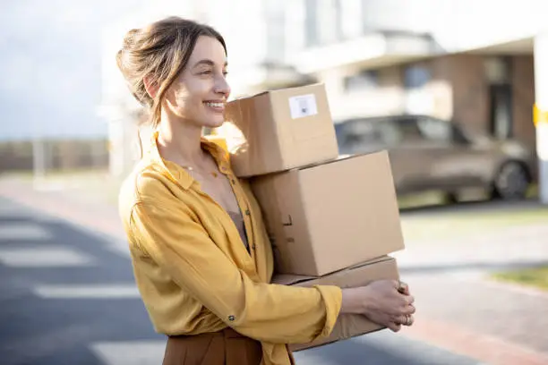 Young happy woman carries home a parcels with goods purchased online at the modern residential district. Concept of online shopping and delivery