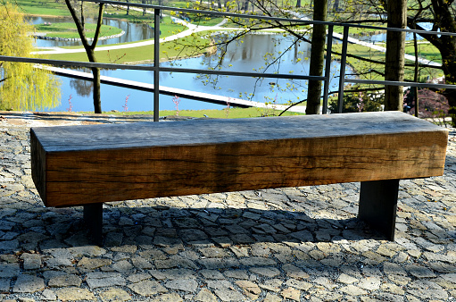 wooden massive park bench shape block with metal legs on granite natural cobblestone irregular brown gray pavement on pedestrian zone oak wood prism painted from one piece trunk
