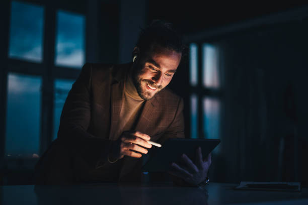 Positive male designer using tablet in dark workplace