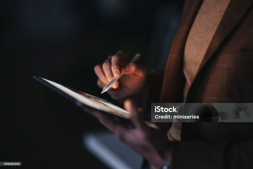 Crop man with stylus using tablet for work at night Unrecognizable male designer using stylus to draw sketch on tablet while working on design project in dark office at night Digital Tablet Stock Photo