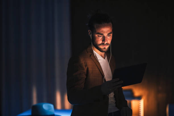 istock Serious man in earphones using tablet in dark room 1316264331