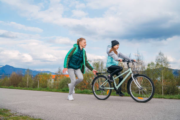 istock Smiling kids on a bicycle asphalt way. Brother helping to sister and teaching doing first steps in riding. Happy childhood concept image. 1316267778