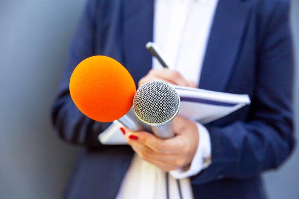 istock Microphone in focus, female journalist at press conference writing notes. Public relations (PR) concept. 1316268722