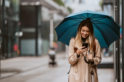 Hermosa chica con un paraguas de pie bajo la lluvia escribiendo un mensaje. photo