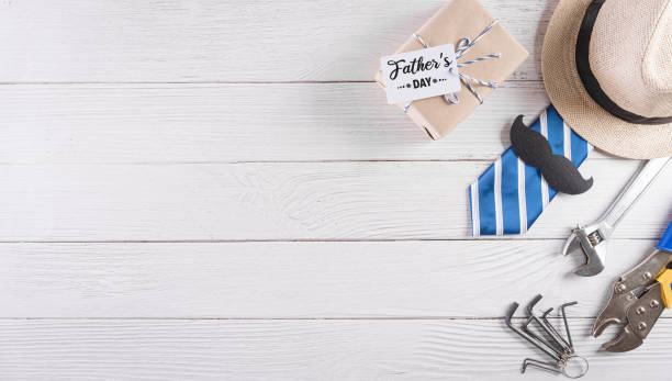 istock Happy Father's Day decoration with beautiful tie with mustache, hand tools, glasses, gift box and hat on white wooden background. 1316272014