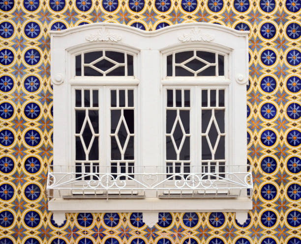 Olhao, Faro District, Portugal: traditional Portuguese tiles (Azulezos) on the wall of a 19th century building with a ornate double window - glazed ceramic tilework with floral pattern.