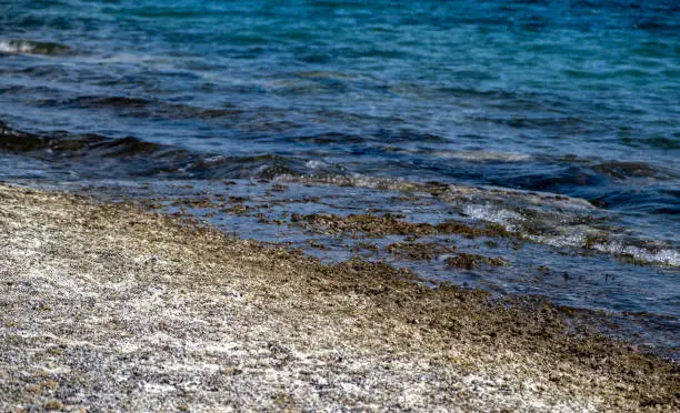 Dry crystal salt on rocky beach. Saline seafront wild beach, healthy, natural salt, medicine, relaxation, nature. Summer destination, tourism at Greek islands. Blue calm sea background.