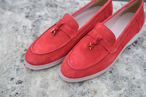 Woman's red stylish suede loafer shoes on the stone background. Pair of trendy female loafers shoes, outdoors.