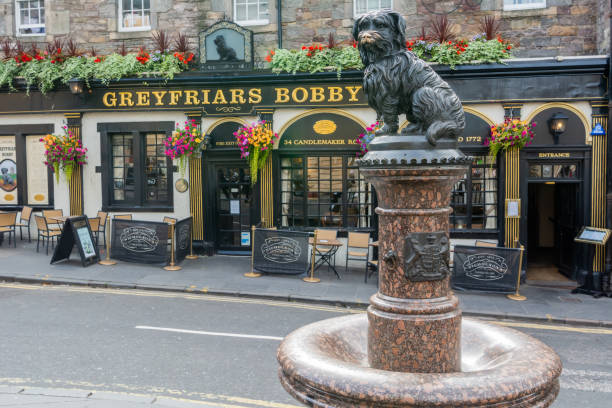 Greyfriars Bobby statue on Candlemaker Row street in Edinburgh, Scotland. Edinburgh, United Kingdom - September 8, 2017. Greyfriars Bobby statue on Candlemaker Row street in Edinburgh, with Greyfriars Bobby bar behind it. midlothian scotland stock pictures, royalty-free photos & images
