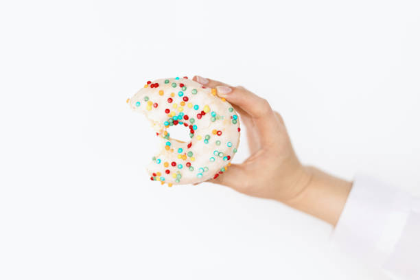 Hand holding bitten delicious donut on background of white wall in room. Birthday party. Diet