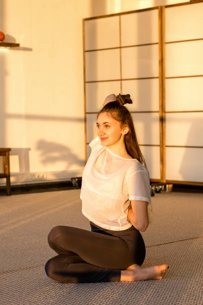 привлекательная девушка сидит в расширенной связаны lotus йога позировать на рассвете в студии йоги. концепция здорового образа жизни - cow face pose стоковые фото и изображен�ия