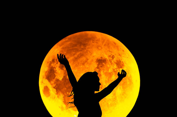 Silhouette of a woman standing in the night with the arms up, giant moon in the background