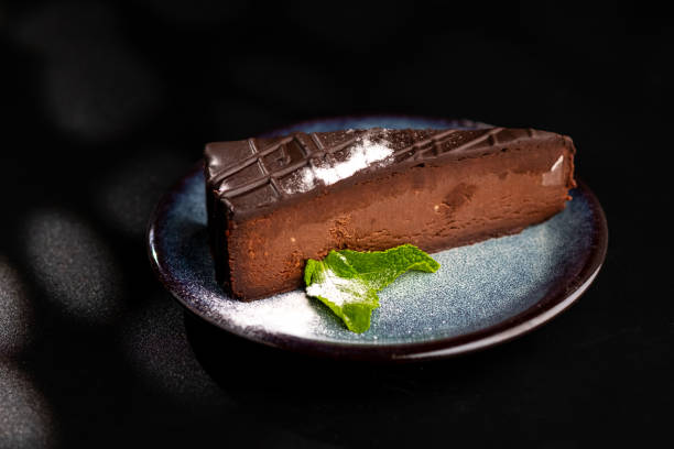 青い皿の上にチョコレートチーズケーキの一部, 粉砂糖とミントの葉で飾られています.黒の背景。 - chocolate cheesecake ストックフォトと画像