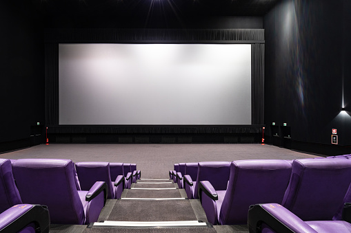 Empty big movie theater hall with a white screen for copy space. Wide angle view of the purple seats and the room, looking at the screen.